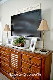 a tv mounted on top of a wooden dresser next to two lamps and a lamp