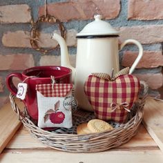 a basket with two mugs and some cookies in it next to a teapot