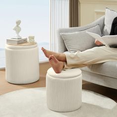 a woman sitting on top of a white ottoman in a living room next to a window