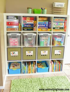 a white bookcase filled with lots of books and bins next to a green rug