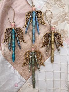 four ornaments are hanging on a piece of fabric with beads and chains attached to them