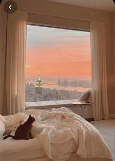 a cat sitting on top of a bed looking out a window at the city skyline