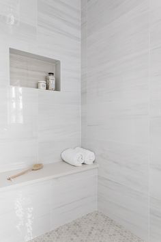 a white tiled bathroom with towels on the shelf and other items in the bathtub