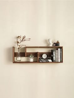 a shelf with books and vases on top of it next to a white wall