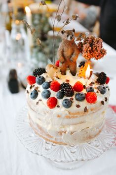 a cake with berries, raspberries, and a teddy bear on top sitting on a table