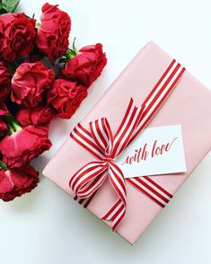 a pink gift box with a red ribbon tied around it next to some red roses