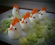 some white eggs with orange heads and lettuce on a plate in the shape of chickens