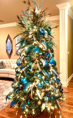 a christmas tree is decorated with blue and green ornaments, lights and feathers on it