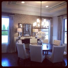 a dinning room table with white chairs and chandelier in front of two windows