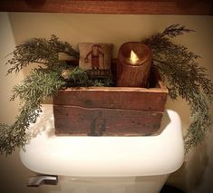 a wooden box filled with greenery sitting on top of a white toilet bowl next to a candle