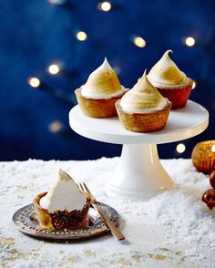 three cupcakes sitting on top of a white cake plate next to some nuts