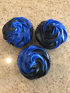 three cupcakes with blue frosting sitting on a counter