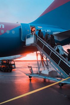 people boarding an airplane at sunset on the tarmac with luggage being loaded onto it