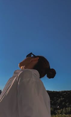 a woman in white shirt and sunglasses looking up into the sky