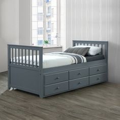 a gray bed with drawers underneath it in a white room next to a window and pictures on the wall