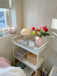 a shelf with flowers and other items on it in a room next to a window