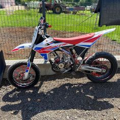 a red, white and blue dirt bike parked next to a fence