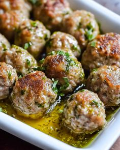 some meatballs are in a white dish with olive oil and parsley on the side