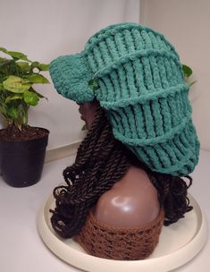 a knitted hat on top of a mannequin's head next to a potted plant