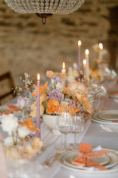 an elegant table setting with candles and flowers in vases on the centerpiece, along with other place settings