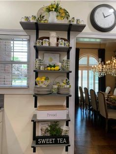 a shelf with plates and cups on it next to a clock in the dining room