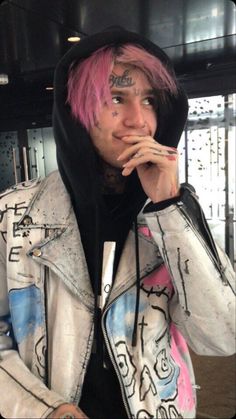 a man with pink hair wearing a white jacket and black hoodie is holding his hand to his mouth