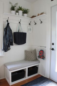 a white bench sitting under a window next to a coat rack and potted plant