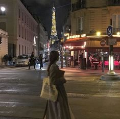 a woman is walking down the street in front of the eiffel tower at night