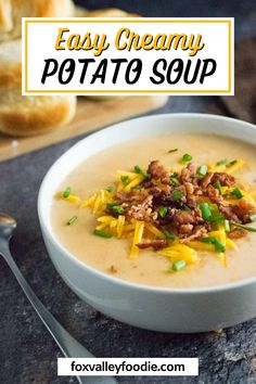 a bowl of creamy potato soup with green onions and bacon on top, next to a loaf of baguette bread