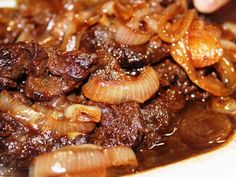 a close up of food on a plate with meat and onions in sauce, being held by a person's hand