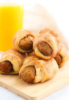 several sausage rolls on a cutting board next to a glass of orange juice