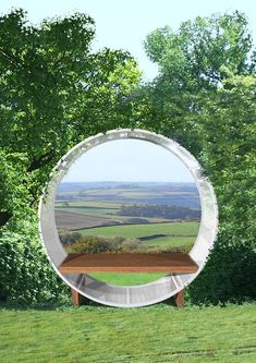 there is a bench in front of a circular mirror on the side of a hill