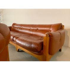 a brown leather couch and chair sitting next to each other in front of a white wall