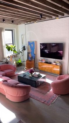 a living room filled with pink furniture and a flat screen tv mounted on the wall