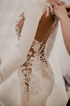 the back of a woman's wedding dress is being fitted with lace and beads