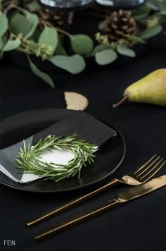 a black plate topped with green leaves next to a knife and fork on top of a table