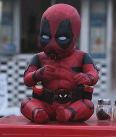 a deadpool doll sitting on top of a red table next to jars and bottles