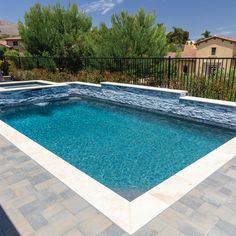 an empty swimming pool in the middle of a backyard with stone pavers and black iron fence