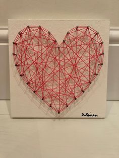 a string art heart is displayed on a white canvas with red thread in the shape of a heart