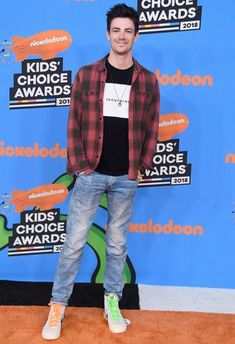 a young man in plaid shirt and jeans at the kids'choice awards on an orange carpet