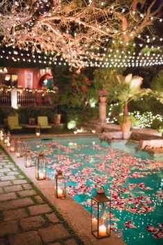 candles are lit in front of an outdoor pool with flowers and lights on the water