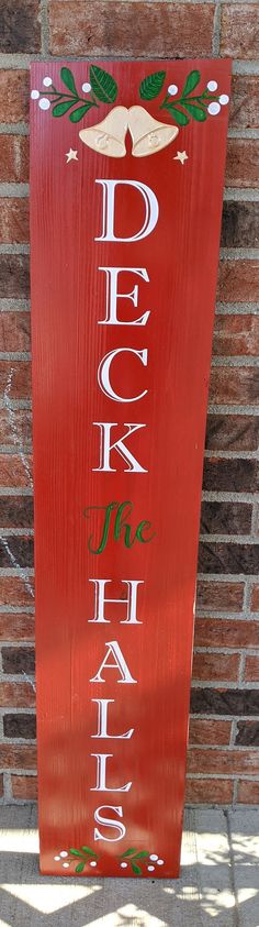 a red wooden sign that says deck the hall on it's front porch with bells and holly leaves