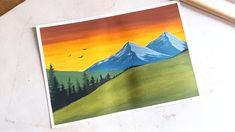 a painting of mountains and trees on a white surface with pencils next to it