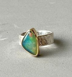 This is a very beautiful opal. It has blue, green and some red and yellow flash. The opal is 16 x 10mm, and wrapped in an 18k gold bezel. Set on a sterling silver band with cross hatch Florentine style. The band is 1/4" wide and a size 6. Unique Green Opal Ring, Opal Jewellery, Luxury Handmade Ethiopian Opal Ring, Gold Ethiopian Opal Cabochon Ring, Ethiopian Opal Silver Gemstone Rings, Unique Ethiopian Opal Cabochon Rings, Elegant Ethiopian Opal Ring, Oval Cabochon, Red Opal, Blue Opal Ring