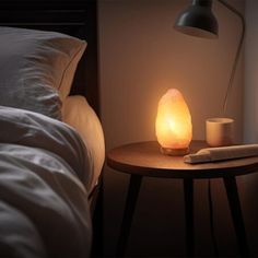 a lamp that is on top of a table next to a bed with pillows and blankets