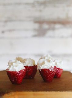 three strawberries with whipped cream on them sitting on a cutting board next to a white brick wall