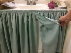 a person is opening the curtain in front of a sink with a flower on it