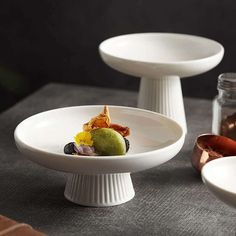 two white dishes with fruit on them sitting on a table