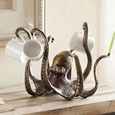 an octopus sculpture holding two cups on it's back legs, with a green toothbrush in its mouth