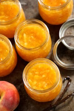 four jars filled with peaches sitting on top of a table next to an apple